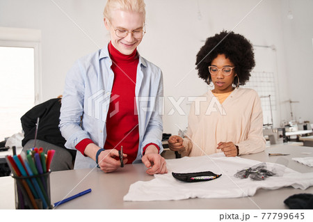 Woman looking attentively at the t shirt and listening ideas from her colleague Woman looking attentively at the t shirt and listening ideas from her colleague 77799645