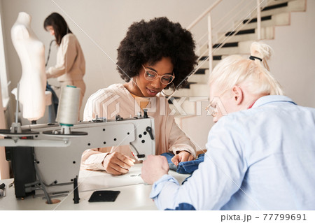 Woman wearing glasses working carefully at the re sewing jeans 77799691
