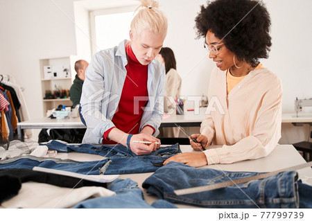 Colleagues cutting clothes while re sewing old products at the table Colleagues cutting clothes while re sewing old products at the table 77799739