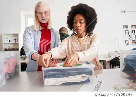 Woman sticks a recycling symbol on a plastic box with a sorting clothes 77800247