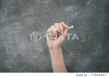 Stop drug addiction concept. Young human hand crushing white pills and syringe with fist over concrete wall background. International Day against Drug Abuse. 77800947