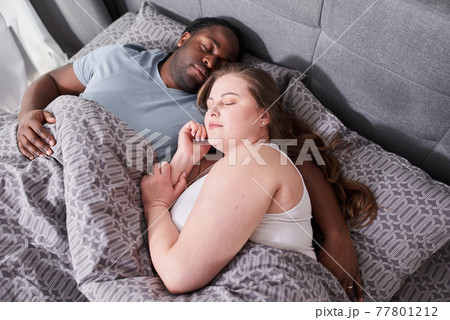 Multiracial couple laying at the bed indoors at home and hugging while sleeping 77801212