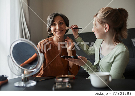 Woman looking at the mirror with pleasure while her granddaughter preparing makeup for her 77801293