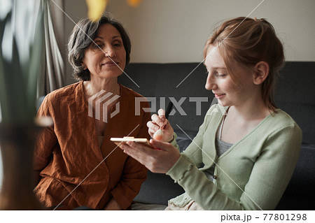 Woman sitting at the full readiness and waiting while her granddaughter preparing makeup for her Woman sitting at the full readiness and waiting while her granddaughter preparing makeup for her 77801298