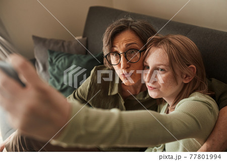 Woman making funny faces with her freckled granddaughter while taking selfie at home Woman making funny faces with her freckled granddaughter while taking selfie at home 77801994
