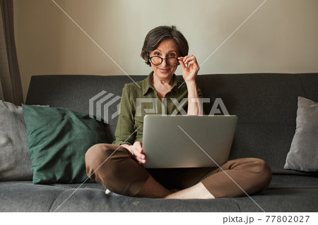 Woman looking at the camera and adjusting her glasses while using laptop 77802027