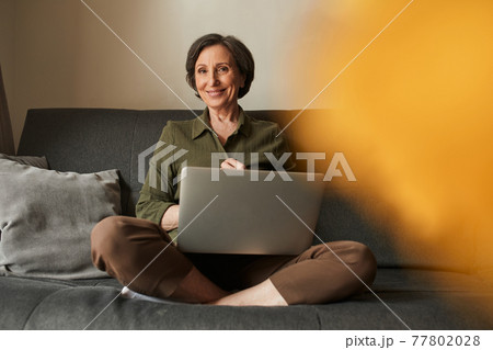 Woman sitting at the lotus pose and holding laptop at the knees while using Internet 77802028