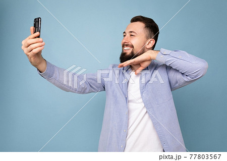 Handsome young brunet bearded man wearing casual stylish clothes standing isolated over blue Handsome young brunet bearded man wearing casual stylish clothes standing isolated over blue 77803567