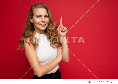 Photo of attractive amazed surprised young woman pointing finger up at copyspace presenting ads 77804171
