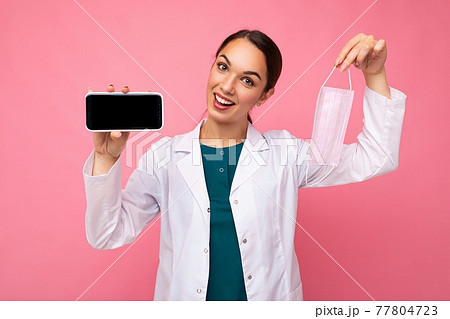 Closeup photo of smiling happy Attractive medical young woman wearing white coat holding mask 77804723