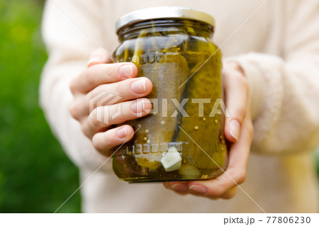 Woman housewife hand holding glass jar of pickled cucumbers. Domestic preparation pickling and canning of vegetables, winter organic food. Healthy fermented homemade food marinated cucumbers in jar. Woman housewife hand holding glass jar of pickled cucumbers. Domestic preparation pickling and canning of vegetables, winter organic food. Healthy fermented homemade food marinated cucumbers in jar. 77806230