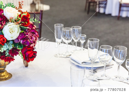 Fancy table set for dinner with flower composition in restaurant, luxury interior background. Wedding elegant banquet decoration and items for food arranged by catering service on white table. Fancy table set for dinner with flower composition in restaurant, luxury interior background. Wedding elegant banquet decoration and items for food arranged by catering service on white table. 77807028