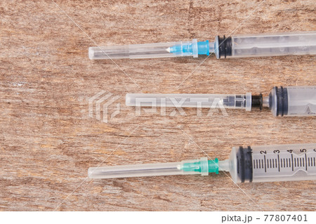 Injection needle syringes, wooden background. 77807401