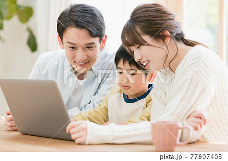 リビングのテーブルに座ってパソコンを見る若い家族 リビングのテーブルに座ってパソコンを見る若い家族 77807403
