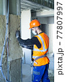 Male builder in mask putting foam into drywall 77807997