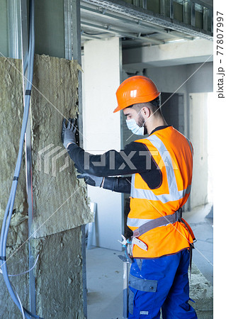 Male builder in mask putting foam into drywall 77807997