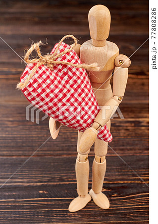 Wooden dummy holding red checkered heart. Wooden dummy holding red checkered heart. 77808286