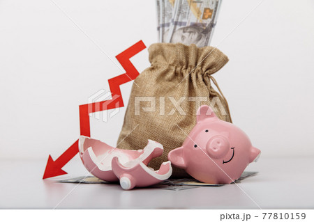 Money bag, broken piggy bank and red down arrow. Stagnation, recession, declining business activity, falling wealth 77810159