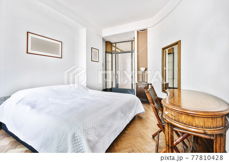 Spacious bedroom with bed and wooden table Spacious bedroom with bed and wooden table 77810428
