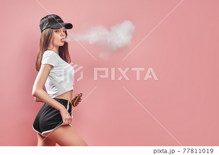 Seductive glamour young woman standing and vaping on pink background 77811019