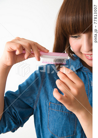 髪の毛先をブラシで梳かす若い女性 77813007