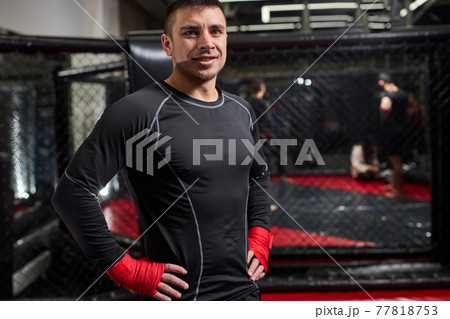 Positive man in the ring in red boxing bandages preparing for battle, smiling at camera 77818753
