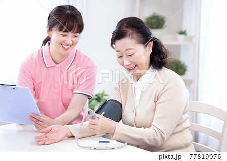 介護　血圧を測るシニア女性と介護士 77819076