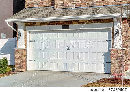 Home with driveway leading to hinged white garage door against stone brick wall 77820607