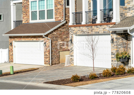 White garage doors and balcony at the facade of homes with stone brock walls 77820608