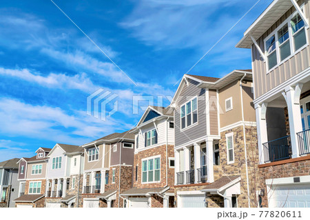 Row of beautiful houses on a peaceful neighborhood set against cloudy blue sky Row of beautiful houses on a peaceful neighborhood set against cloudy blue sky 77820611