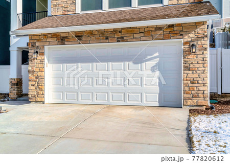 Wide white garage door of an attached garage of home with stone brick wall 77820612