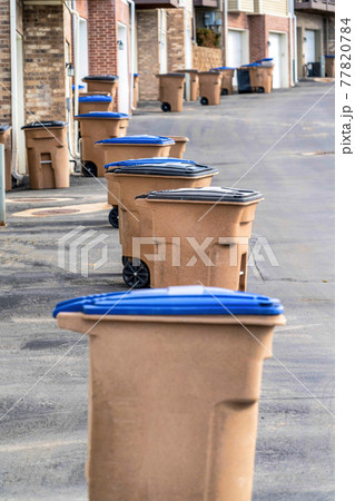 Grabage bins with wheels in front of townhouses along a paved neighborhood road 77820784
