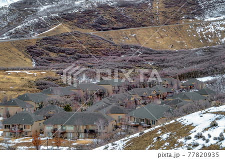 Group of houses sitting on a mountain terrain dusted with white snow in winter Group of houses sitting on a mountain terrain dusted with white snow in winter 77820935