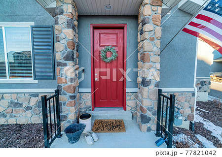 Red front door with wreath and portico with stone columns at the home entrance 77821042