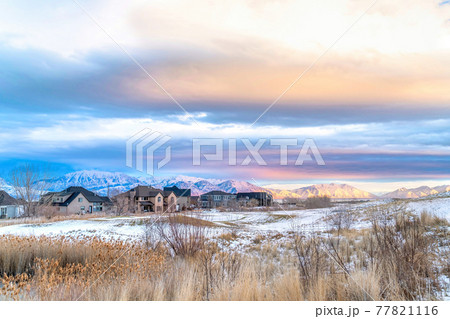 Sunset view of snowy valley in winter with homes against sunlit frosted mountain Sunset view of snowy valley in winter with homes against sunlit frosted mountain 77821116