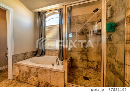 Warm toned bathroom with round bathtub tiles shower stall and arched window 77821195