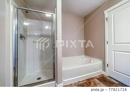 Shower stall and bathtub inside a clean bathroom with brown tiles on the floor 77821728
