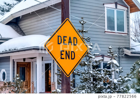 Bright dead end road sign on a post with gray home exterior in the background Bright dead end road sign on a post with gray home exterior in the background 77822566