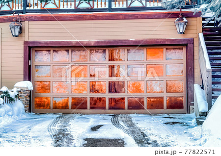 Panelled metal garage door of home beside stairs that leads up to snowy balcony Panelled metal garage door of home beside stairs that leads up to snowy balcony 77822571