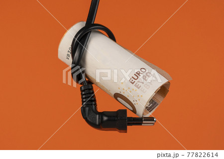 Euro money in an electrical cord knot with a plug close up. Home finance concept. Cash banknotes. On a colored creative terracotta orange background. The savings and high cost of household electricity Euro money in an electrical cord knot with a plug close up. Home finance concept. Cash banknotes. On a colored creative terracotta orange background. The savings and high cost of household electricity 77822614