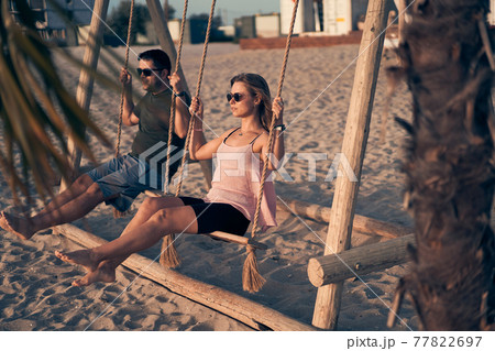 Young attractive couple swinging on seesaw on the beach. Young attractive couple swinging on seesaw on the beach. 77822697
