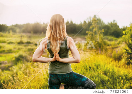 A young woman performs a yoga asana outdoors. Rear view, space for text. Yoga, fitness, sports 77825063