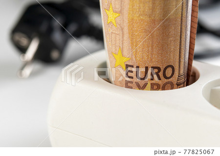 Fifty euro banknote in a white extension cord outlet on the background of wires and plug in blur. Macro. Home electricity purchase and budget saving efficiency concept 77825067