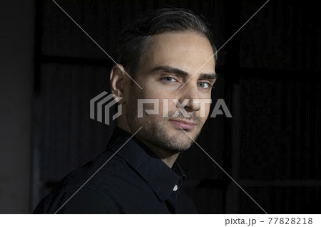 An influencer, artist and musician, dress with black shirt, poses for the camera in one of his photographic shootings for social networks, in a dark backstage area, at night, in Spain. An influencer, artist and musician, dress with black shirt, poses for the camera in one of his photographic shootings for social networks, in a dark backstage area, at night, in Spain. 77828218