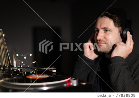 Young handsome millennial guy listens to music with headphones on dark bakdrop Young handsome millennial guy listens to music with headphones on dark bakdrop 77828909