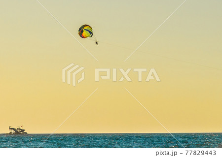 Man and woman tourists are flying on a parachute over the sea against the backdrop of the sunset sky and the horizon. Extreme vacation concept 77829443