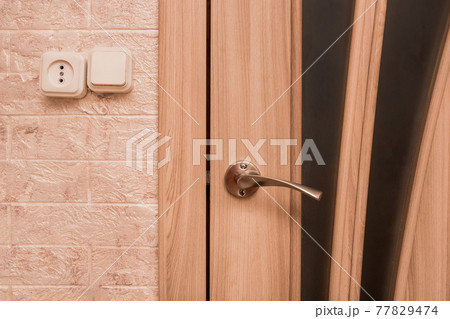 Part of the interior of a modern living room with an iron doorknob, socket and light switch close-up Part of the interior of a modern living room with an iron doorknob, socket and light switch close-up 77829474
