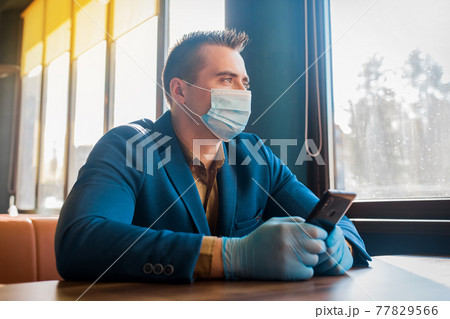 Caucasian male businessman in protective gloves and medical mask spends time in mobile phone in cafe 77829566