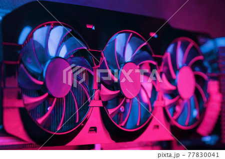 A graphics card with a row of fans with a cyanotic purple backlight in a futuristic design. A graphics card with a row of fans with a cyanotic purple backlight in a futuristic design. 77830041