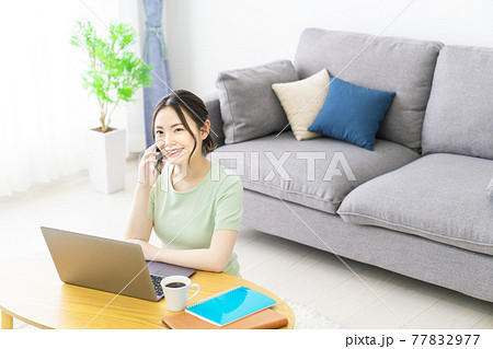 自宅でテレワークをしながらスマホで電話する女性 77832977